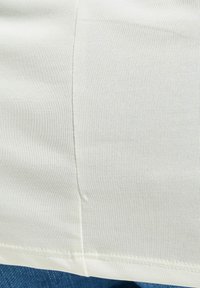 Lys beige stoff med en jevn tekstur, som har fine ribber og en rett kant. Synlig søm langs siden.