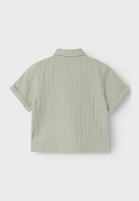 Camicia a maniche corte con colletto di colore verde chiaro, realizzata in un tessuto morbido e texturizzato, con una lunghezza cropped, maniche arrotolate e orlo dritto.