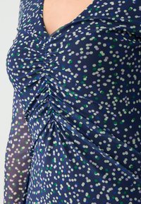 Abito della marina con design arricciato, caratterizzato da un motivo a pois in verde, viola e bianco. Tessuto trasparente con una consistenza morbida.