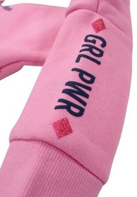 Pull en rose avec des poignets côtelés, arborant le texte bleu marine "GIRL PWR" et un accent en diamant rouge pailleté près du texte. Texture de tissu douce.