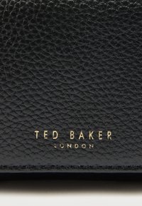 Czarny skórzany portfel o teksturowanej powierzchni. Złote tłoczone logo „TED BAKER LONDON” na dole.