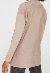 Jasnobeżowy sweter z długim rękawem, z teksturowanym, prążkowanym wzorem na ramionach i plecach, z kołnierzykiem i luźnym krojem.