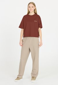 Brun kortärmad t-shirt med texten "LES ARCS" tryckt på bröstet, kombinerad med beige, löst sittande sweatpants och beige sneakers. Enkelt design.