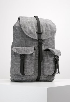 Sac à dos en tissu gris avec deux poches avant et fermetures à boucle verticale noires sur une surface blanche.