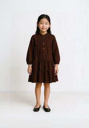 Ruskea leopardi-kuosis mekko, jossa on pyöreä kaulus, nappikiinnitys ja puffihihat. Mekossa on liehuvahelma, jossa on kerroksittain frillaa. Mustat ballerinat.