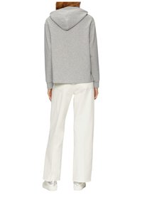 Felpa grigia con cappuccio foderato, abbinata a pantaloni bianchi a gamba larga. L'outfit presenta una vestibilità rilassata e un tessuto morbido e testurizzato.