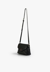 Borsa a tracolla in pelle nera trapuntata con pattina pieghevole, tracolla regolabile e un piccolo accento rosso sul fronte. Presenta una forma strutturata.