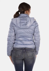 Giacca puffer azzurra chiara con cappuccio, caratterizzata da un'imbottitura orizzontale e una finitura lucida. Il design include una zip color oro e tasche.