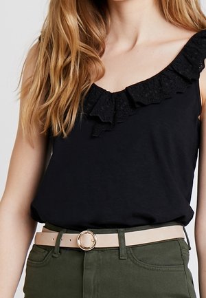 Haut noir sans manches avec un détail volanté texturé le long du décolleté, associé à un pantalon vert taille haute et une ceinture claire avec une boucle ronde.