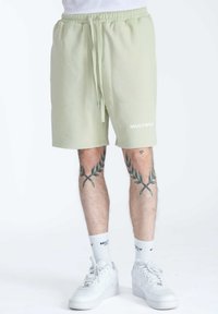 Pantaloni corti in cotone verde chiaro con vita elasticizzata e cordino, con un logo bianco "MULTIPLY" sulla coscia sinistra.