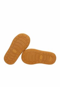 Suole di scarpe in gomma di colore marrone chiaro con motivi testurizzati per la presa. Presentano bordi arrotondati e un logo impresso sulla superficie.
