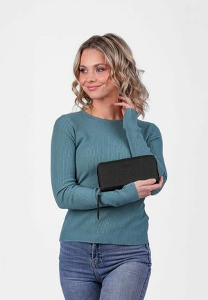 Černá peněženka na zip držena proti tyrkysovému žebrovanému topu s dlouhým rukávem. Peněženka má hladký povrch a minimalistický design.
