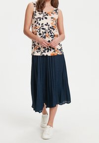 Débardeur fleuri crème, orné de fleurs orange et marine. Associé à une jupe midi plissée marine et des baskets blanches.