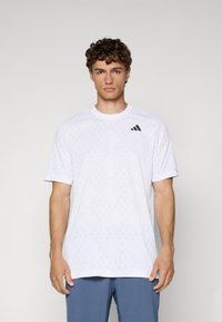 Weißes T-Shirt mit kurzen Ärmeln aus leichtem Material, das ein dezentes Diamantenmuster aufweist und ein schwarzes Adidas-Logo auf der Brust trägt.