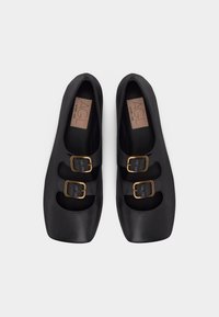 Μαύρα δερμάτινα παπούτσια Mary Jane με τετράγωνες μύτες και δ ιπλές χρυσές αγκράφες, τοποθετημένα δίπλα-δίπλα σε λευκό φόντο.