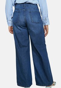 Wijdvallende blauwe denim jeans met een hoge taille, voorzien van twee achterzakken en een strakke afwerking. De stof heeft een klassieke denimtextuur.
