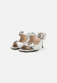 Open-toe hoge hakken van glanzend zilver metallic materiaal, met een gespsysteem en een slanke stilettohak. Vierkante punt ontwerp.