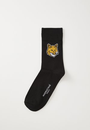 Chaussettes noires en tissu avec une texture côtelée, présentant une tête de renard brodée en jaune et blanc sur le côté.