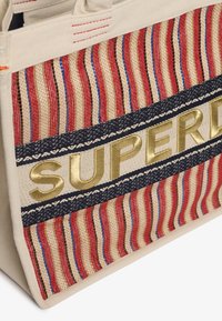 Canvas draagtas met rode en blauwe strepen, een marineband met een wit patroon en gouden "SUPERD" letters op de voorkant.
