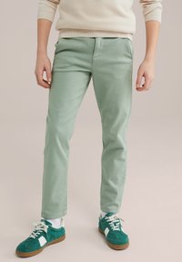 Pantaloni v mint zelenem slogu slim fit, narejeni iz lahkega materiala, z gladko teksturo in klasičnim pet-imernim dizajnom. V kombinaciji z zelenimi športnimi copati.