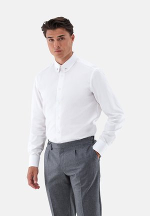 Weißes Langarmhemd mit klassischem Kragen und Knopfdetails, kombiniert mit grauen Hosen mit Plissee-Design und seitlichen Taschen.