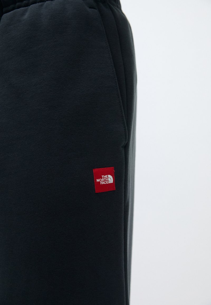 Sorte joggingbukser lavet af blødt stof, med elastisk talje og et lille rødt logo-patch på venstre lår.