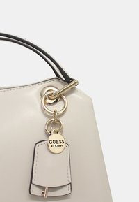 Borsa a mano in pelle crema con design strutturato, dotata di manico nero, hardware dorato e un portachiavi decorativo.