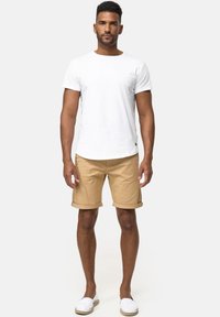 T-shirt en coton blanc, shorts beige retroussés et espadrilles blanches. Design simple, coupe décontractée, texture lisse et sans motifs visibles.