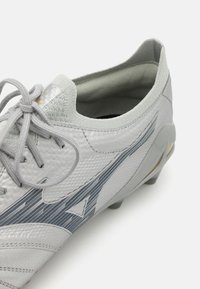 Lichtgrijze voetbalschoen met gestructureerd synthetisch bovenwerk, grijze gestreepte design, ronde veters en een prominente haklip. Rubber noppen op de zool.
