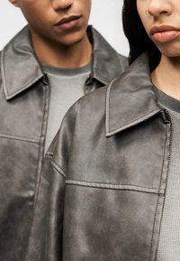 Γκρι δερμάτινο μπουφάν από συνθετικό δέρμα με μυτερό γιακά, με διακριτική υφή και λεπτομερή ραφή, συνδυασμένο με γκρι τοπ με υφή.