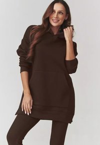 Brązowy pulower z kapturem, z przednią kieszenią, ściągaczami przy mankietach i u dołu. Wykonany z miękkiego materiału, ma luźny krój i mały kołnierzyk.