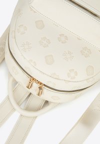 Sac à dos en cuir crème rond avec des motifs embossés, des fermetures éclair dorées et des bretelles plates. Fini texturé avec des accents matériels subtils.