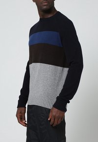 Pull en tricot avec blocs de couleur horizontaux en marine, bleu, marron et gris. Col rond et poignets côtelés, avec une finition texturée.