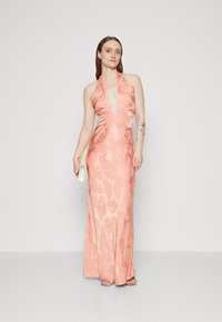 Robe halter en satin de couleur pêche avec un motif de feuilles, corsage ajusté et jupe fluide. Accompagnée d'une pochette blanche.