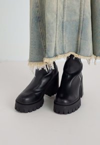 Bottes noires en cuir à la cheville avec des semelles de plateforme épaisses et des talons épais. Le design présente une texture lisse et une fermeture éclair sur le côté.