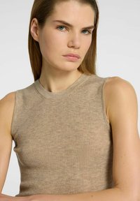 Beige ribbet tanktop med høj hals og ærmeløs design, der fremhæver en blød tekstur og en tætsiddende silhuet.