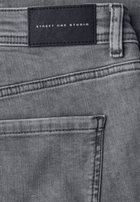 Tissu en denim gris avec une texture lisse ; présente une étiquette en cuir noir avec l'inscription « STREET ONE STUDIO » cousue le long de la ceinture et de la poche arrière.