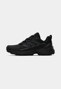 Schwarze Sportschuhe mit einer strukturierten Oberseite, ausgeprägtem Profil an der Sohle und drei kontrastierenden Streifen an der Seite. Mit einer Zuglasche hinten.