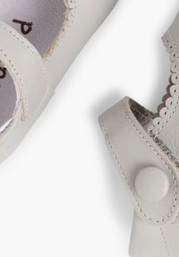 Zapatos de cuero gris con adornos en forma de onda y una correa de gancho y bucle. Punta redondeada y plantilla texturizada visibles desde una perspectiva superior.