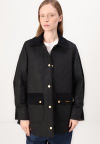 Black quilted jacket with gold snaps and corduroy pockets, featuring a black collar and subtle diamond pattern texture.