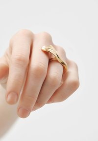 Anillo de oro con un diseño liso y retorcido, con un acabado pulido. El anillo envuelve el dedo y tiene una textura brillante.