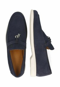 Marineblauwe suède instappers met een zilverkleurig logo-accent, witte rubberen zool en contrasterende stiksels, met een gladde textuur en een instapontwerp.