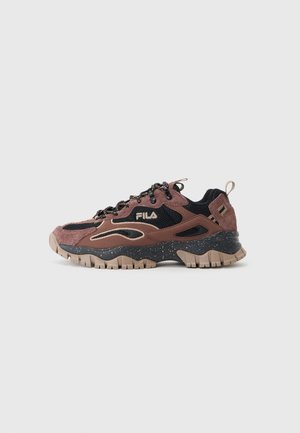 Zapatilla FILA marrón y negra con suela rugosa, parte superior de malla y ante, cordones negros y entresuela moteada vista de lado sobre un fondo gris.