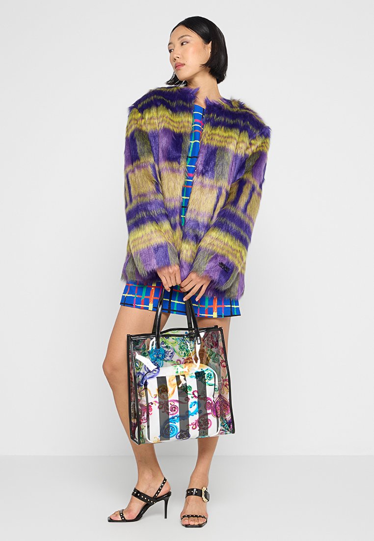 Faux-Fur-Mantel mit lila und grünen Streifen, blaues karierter Kleid, durchsichtige Tragetasche mit bunten Akzenten und schwarze Absatzsandalen.