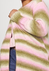 Cardigan en tricot avec des rayures horizontales rose et vert olive, doté d'un col en V profond et d'un devant ouvert. Texture douce avec des fentes sur les côtés.