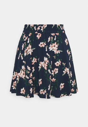 Jupe bleu marine avec motif floral rose et blanc, taille élastique et design plissé, suspendue sur un fond blanc.