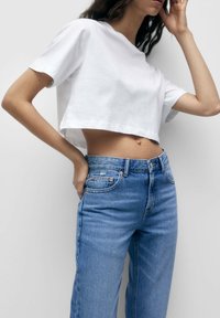 Camiseta blanca de algodón cortada, con mangas cortas y escote redondo, combinada con jeans de mezclilla claros de tiro alto con acentos descoloridos.