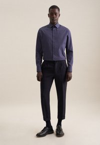Camicia button-up a fantasia navy con colletto, abbinata a pantaloni dark tailored e scarpe lace-up nere. Design semplice, silhouette aderente.