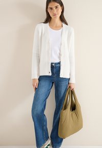 Bílý pletený kardigan s knoflíky, doplněný světle modrými džínami s širokými nohavicemi a měkkou taškou khaki zelené barvy. Hladká textura a neformální design.