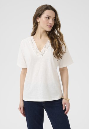 Haut blanc à manches courtes et décolleté en V avec des détails en broderie à œillets le long du col ; tissu doux ; associé à un jean en denim bleu foncé.